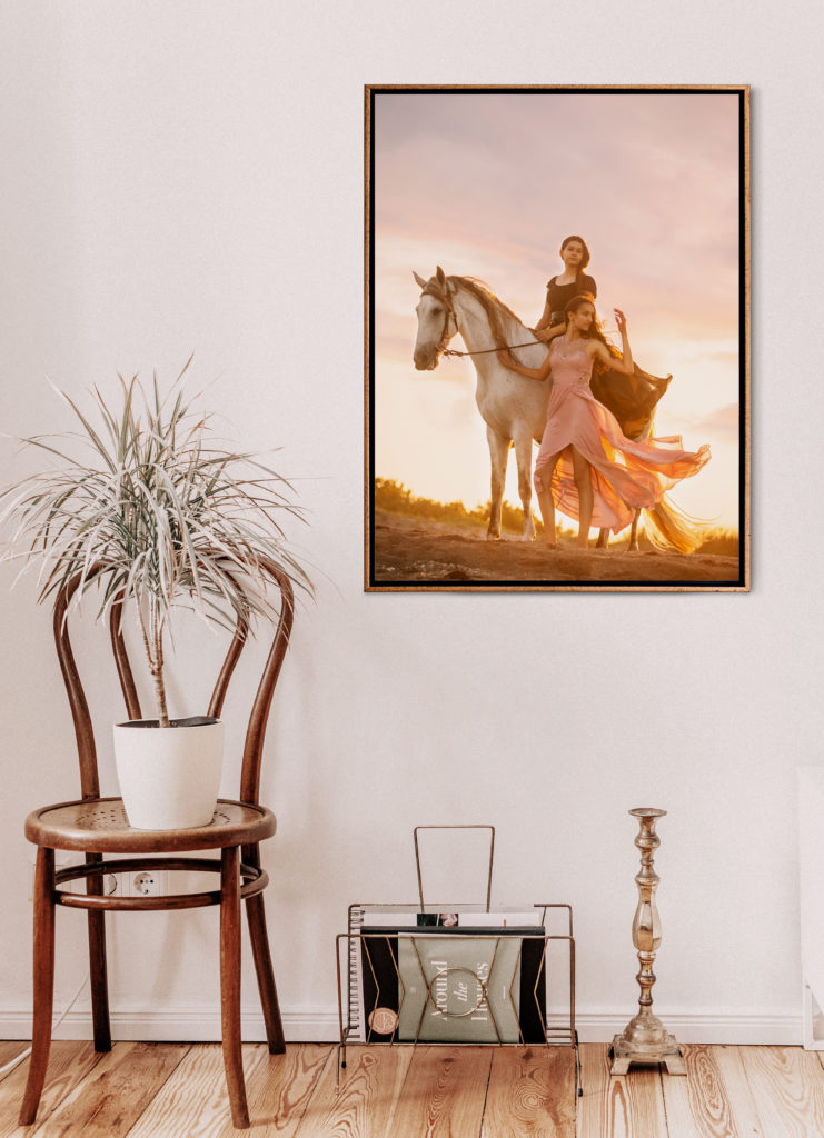 Printed artwork of two girls with a white horse hung on a wall with a table nearby. 