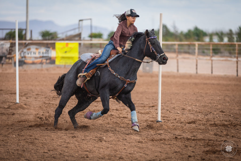 Photograph of a cowgirl riding her horse between vertical poles on the ground.