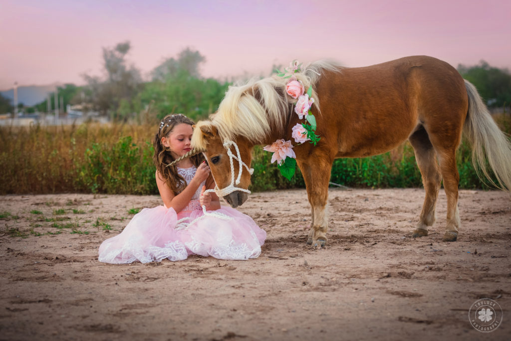 Photograph of a girl wearing a pink dress posing next to a palomino unicorn in El Paso, Texas. 