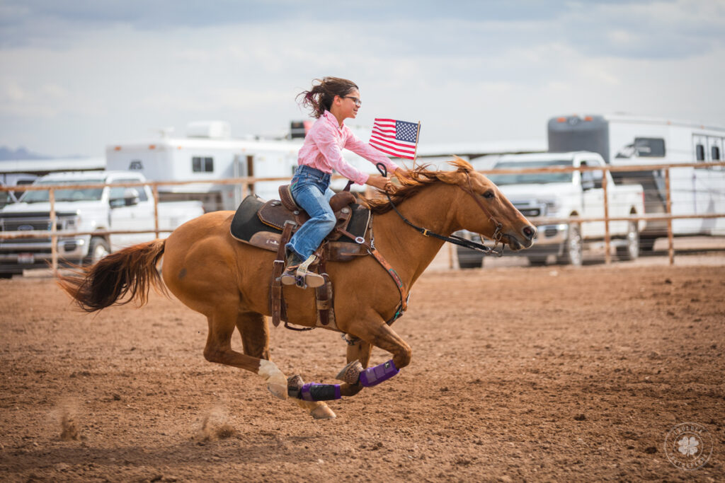 Photograph of a little girl riding a running horse while carrying a small American flag in Deming, New Mexico. 