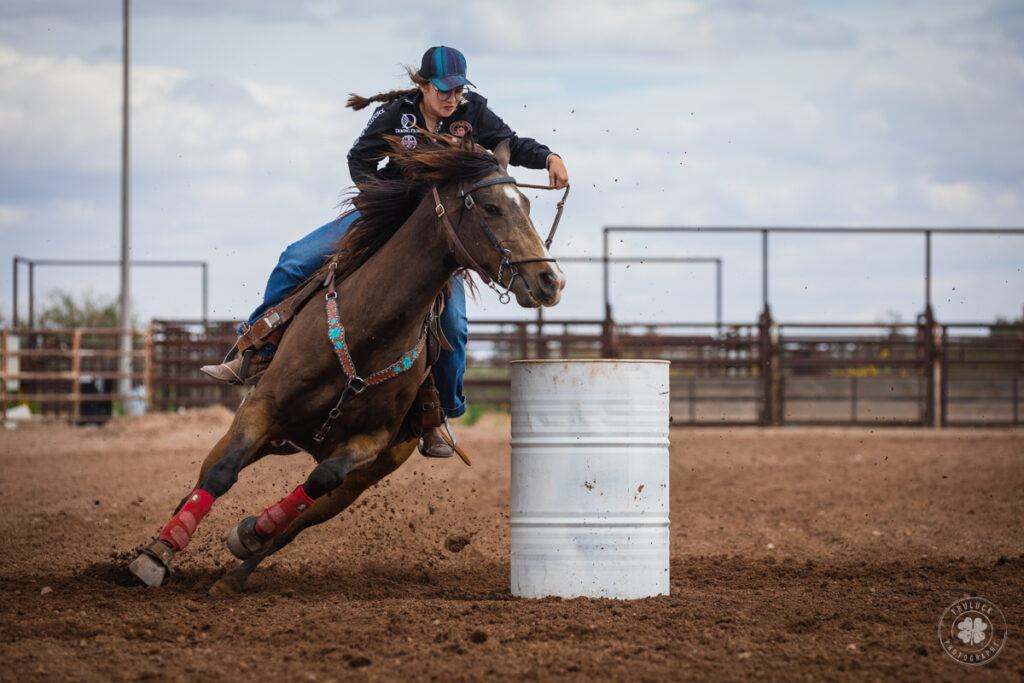 Photograph of a cowgirl guiding her horse around a barrel during a barrel race in Deming, New Mexico. 