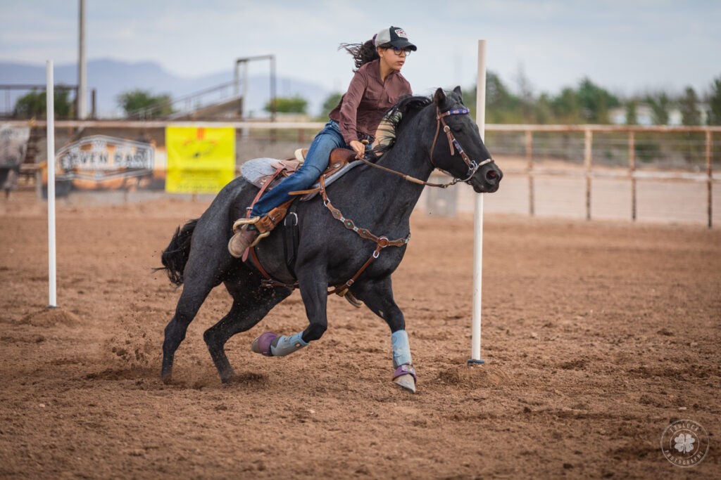 Photograph of a cowgirl riding her horse through poles during a rodeo in Deming, New Mexico.  