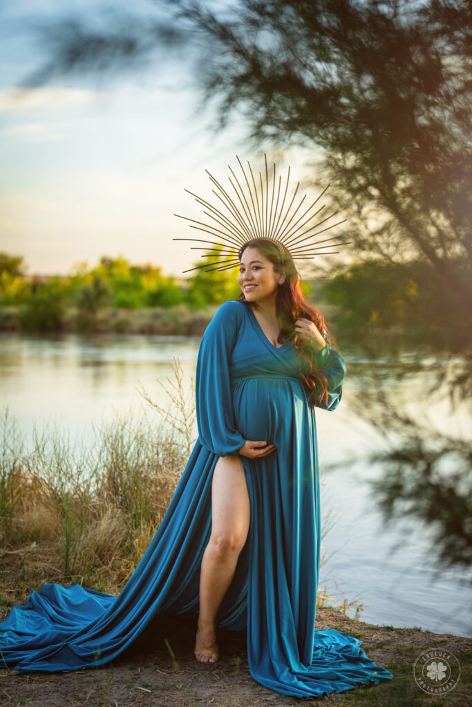 Photograph of a barefoot pregnant woman wearing a blue maternity dress posing on the banks of the Rio Grande in El Paso, Texas.