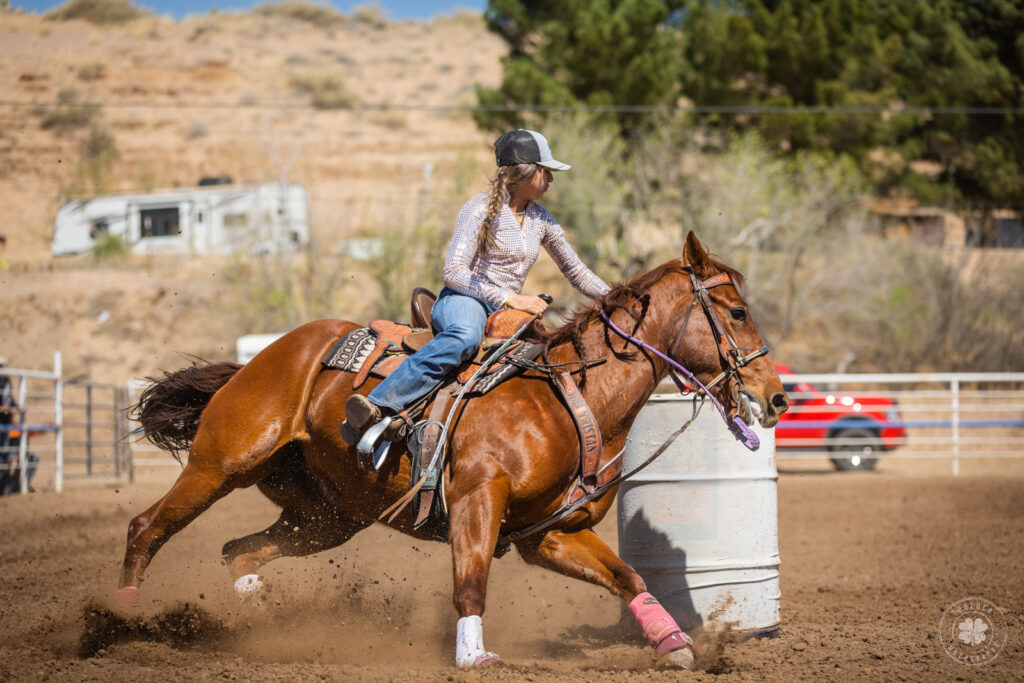 Photograph of a cowgirl riding a horse around a barrel during a horse show in Socorro, Texas. 