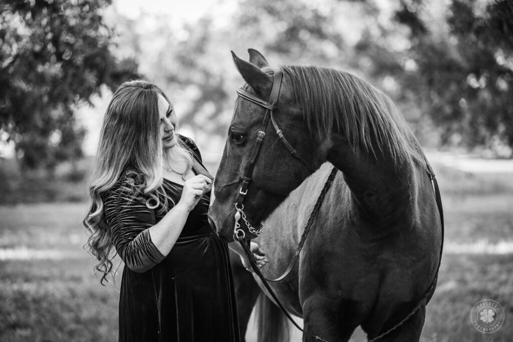 Black and white photograph of a woman wearing a dress petting the nose of a horse.  This was photographed for the 19 Over 19 Project by Truluck Photography. 