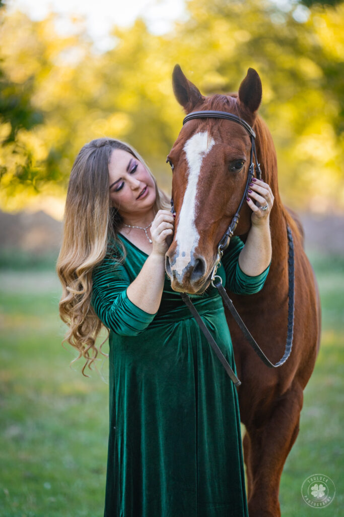 Photograph of a woman in a green dress standing next to a chestnut horse with her hands holding his face in Las Cruces, New Mexico. 
