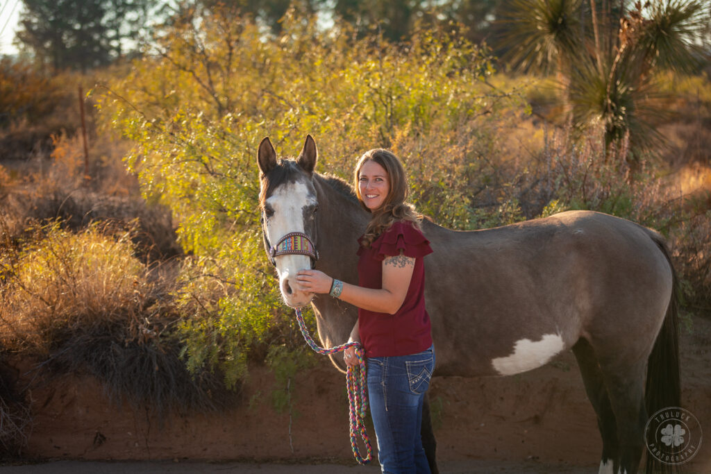 Photograph of a woman wearing jeans and a ruffled red shirt posing with her senior horse.