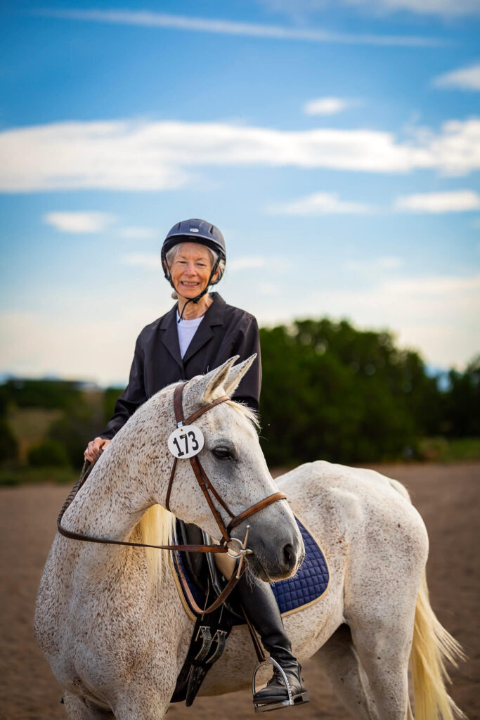 Vertical photograph of a 73 year-old woman riding a gray horse in English show attire in Santa Fe, New Mexico. 