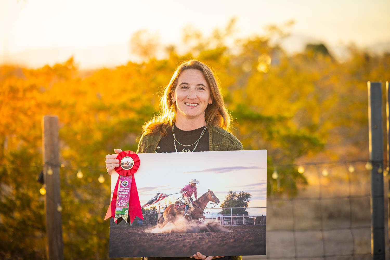 Photograph of a woman holding a metal print of a cowboy riding a spinning chestnut horse while holding the American flag.