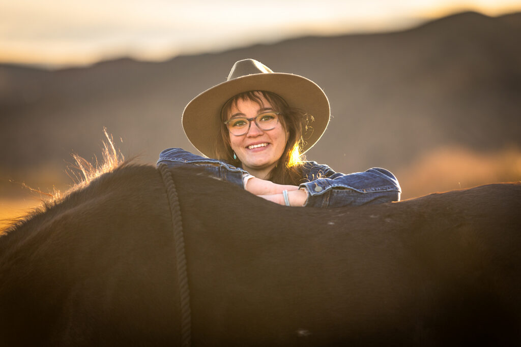 Photograph of a chic cowgirl in a denim jacket with glasses posing against the back of her horse in El Paso, Texas. 