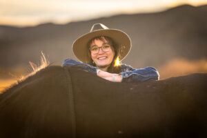 Photograph of a chic cowgirl in a denim jacket with glasses posing against the back of her horse in El Paso, Texas.