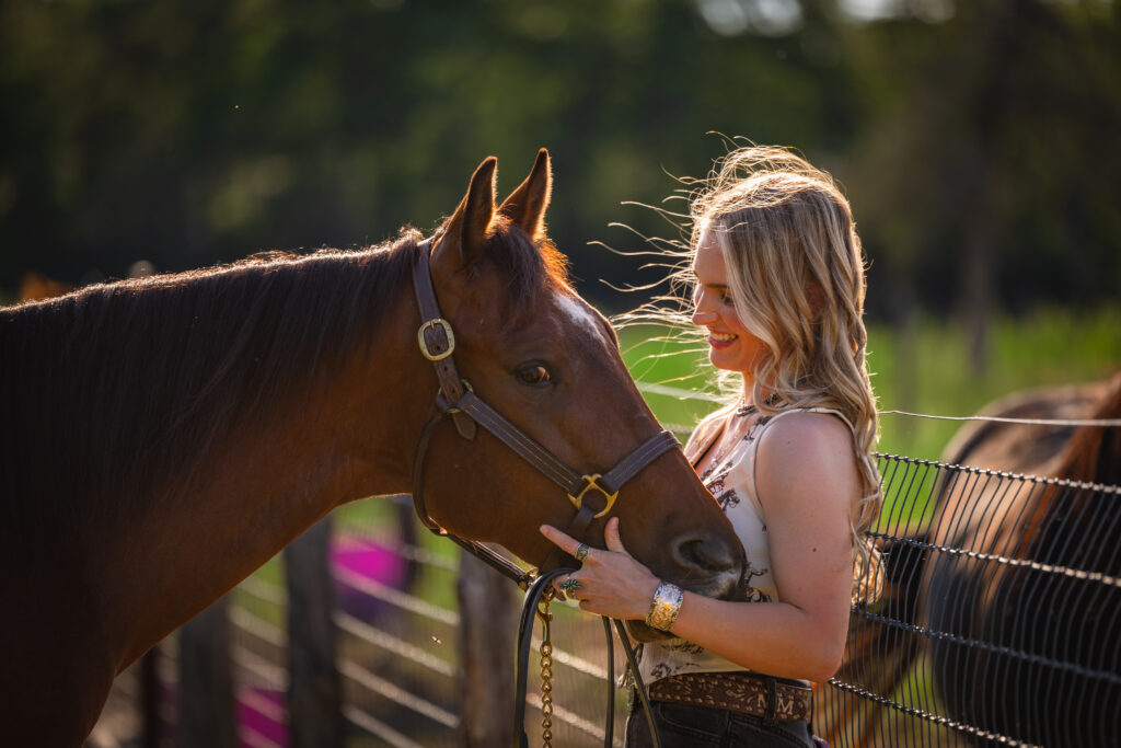 Photograph of a blonde girl holding her bay horse's head as he nuzzles her in College Station, Texas.