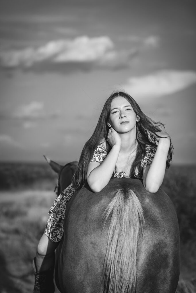 Photograph of a teenager flipping her hair back while laying on the back of her horse