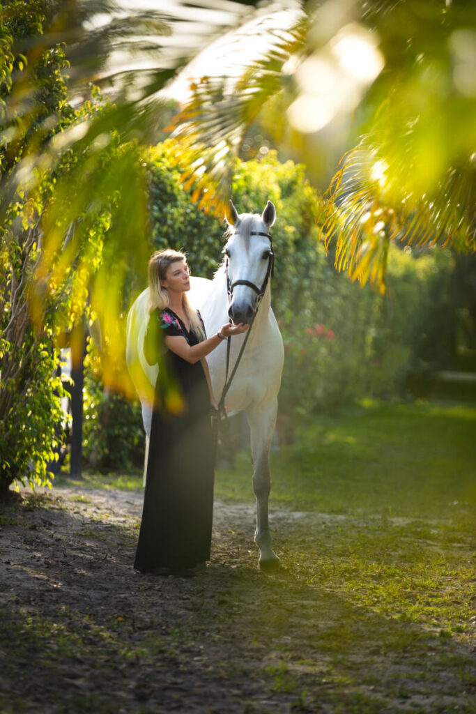 Photograph of a woman petting her gray horse framed by palm trees in Florida